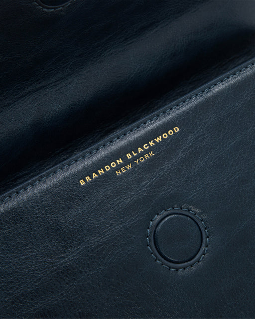 Angled close up of Nia Bag with navy cracked leather with brass logo magnetic closure