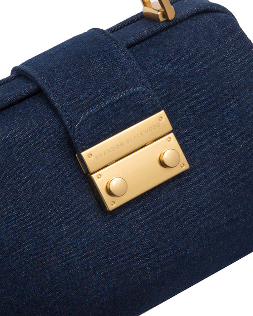 Angled close up of Elizabeth Doctor Bag in dark denim with brass clasp buckle with embossed logo