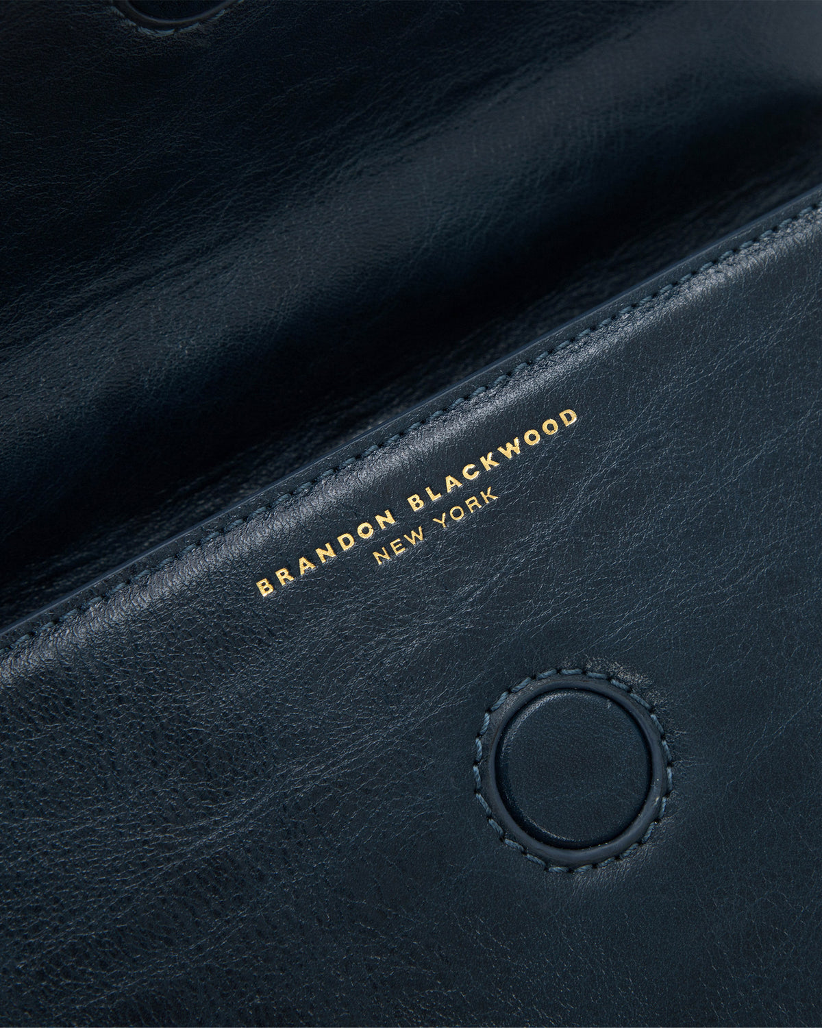Angled close up of Nia Bag with navy cracked leather with brass logo magnetic closure 