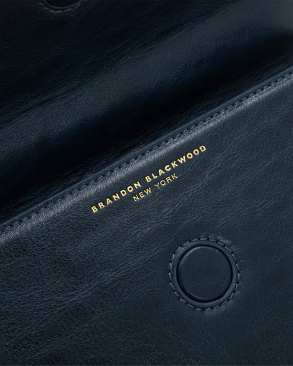Angled close up of Nia Bag with navy cracked leather with brass logo magnetic closure  thumbnail 6