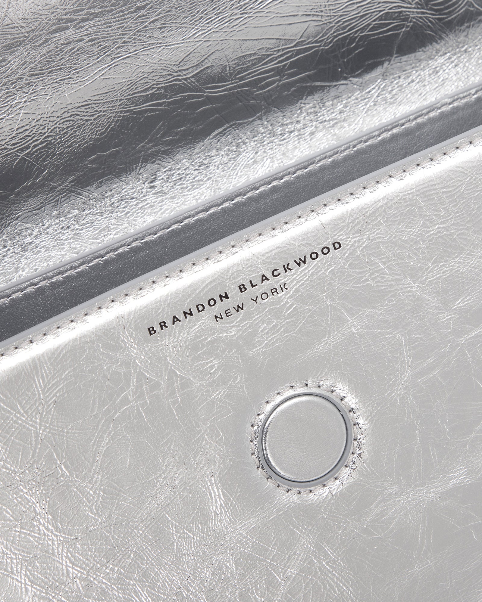 Angled close up of Nia Bag with silver cracked leather with silver logo magnetic closure 