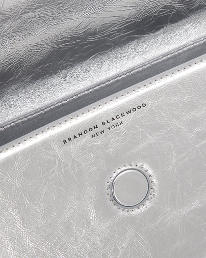 Angled close up of Nia Bag with silver cracked leather with silver logo magnetic closure  thumbnail 5