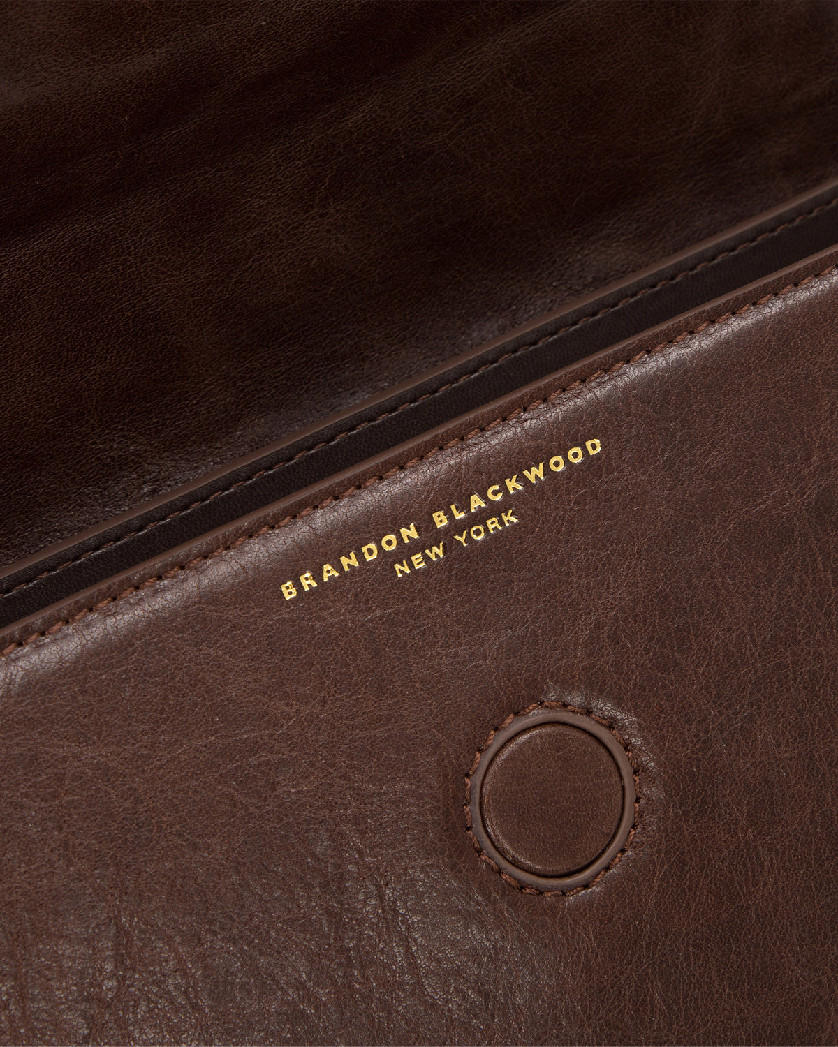 Angled close up of Nia Bag with brown cracked leather with brass logo magnetic closure 