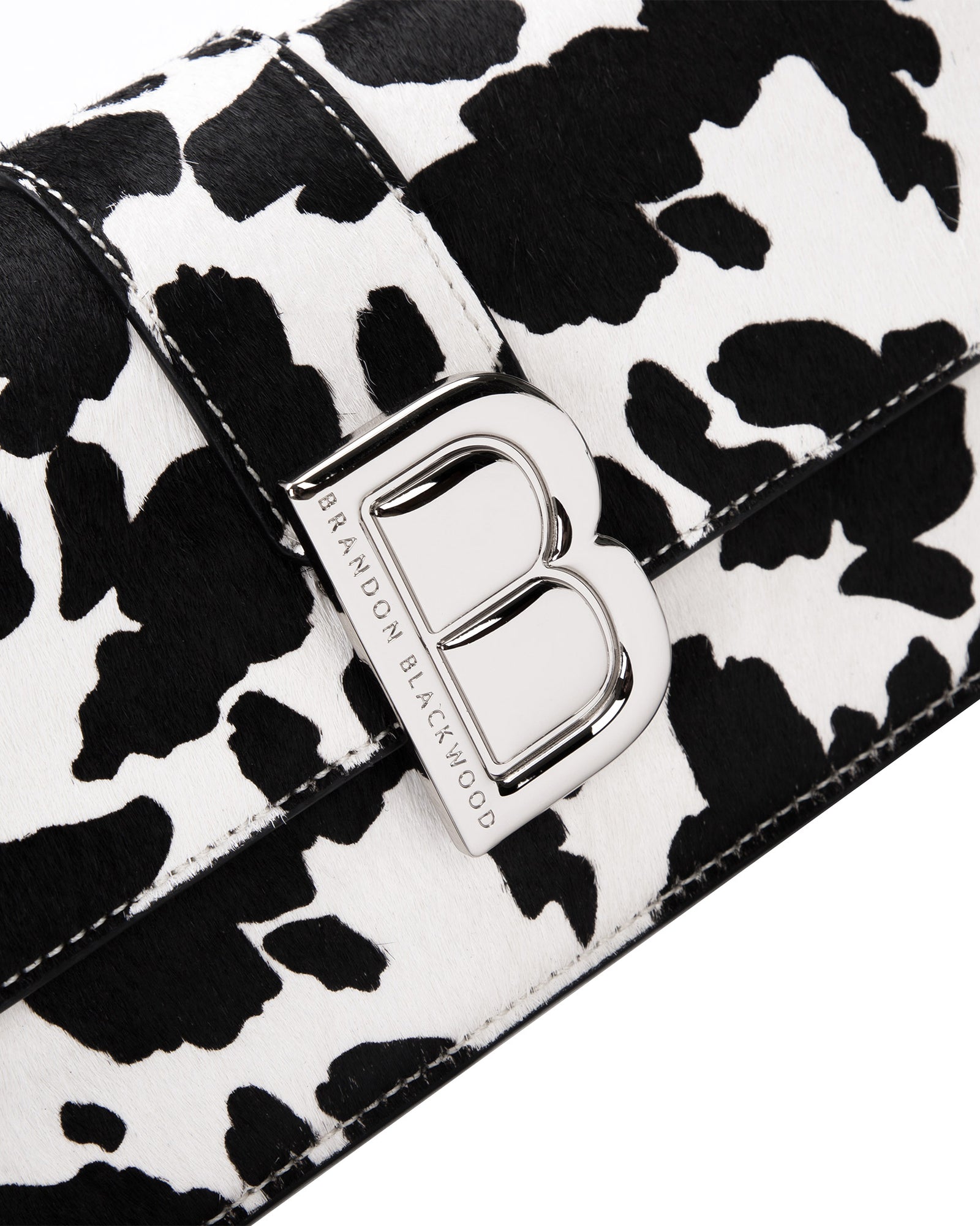 Angled close up of Nia Bag with  black and white cow print with silver logo magnetic closure 