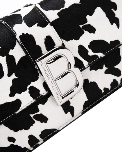 Angled close up of Nia Bag with  black and white cow print with silver logo magnetic closure  thumbnail 3