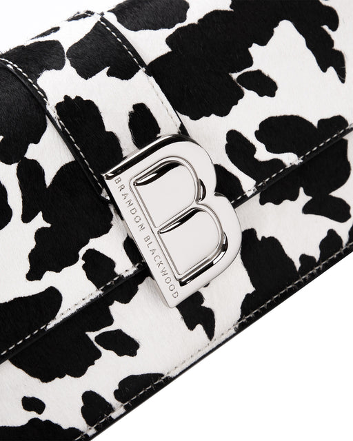 Angled close up of Nia Bag with  black and white cow print with silver logo magnetic closure 