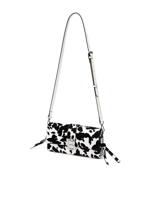 Nia Bag with black and white cow print with cow print strap with silver logo magnetic closure hanging with strap