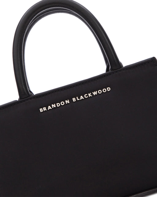 Angled close up of Arlen Bag, black nylon body with leather handle, Brandon Blackwood hardware logo